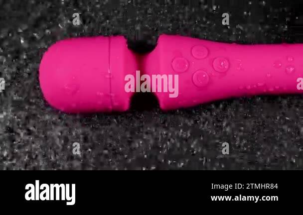 The pink dildo creates a vibration on the surface of the water. Sex toy on  a black background