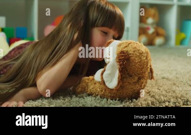 Pretty little girl lying on the floor and kissing and hugging her teddy ...
