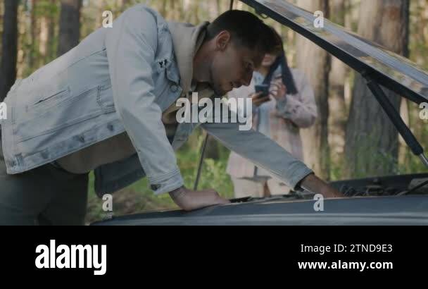 Man repairing broken car while woman calling for emergency service ...