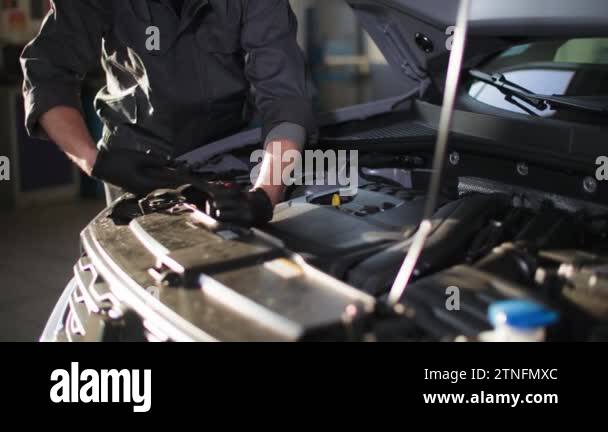 auto maintenance, a young man in uniform repairs car engine with wrench ...