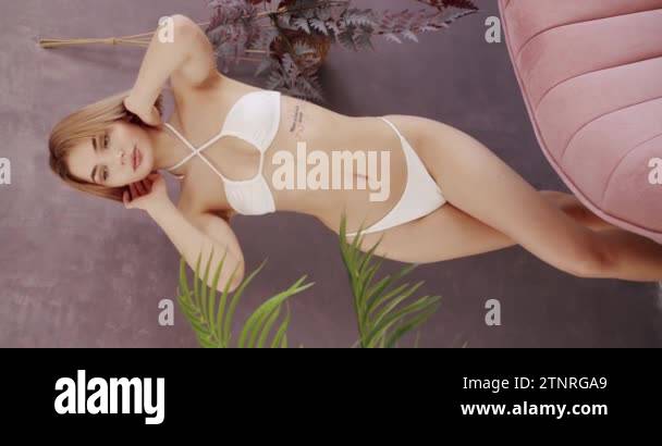Sexy young woman in a white bathing suit posing at home. Attractive woman  in white lingerie. Summer and swimwear concept. Vertical video. Beautiful  woman in bikini swimsuit relaxing at home.