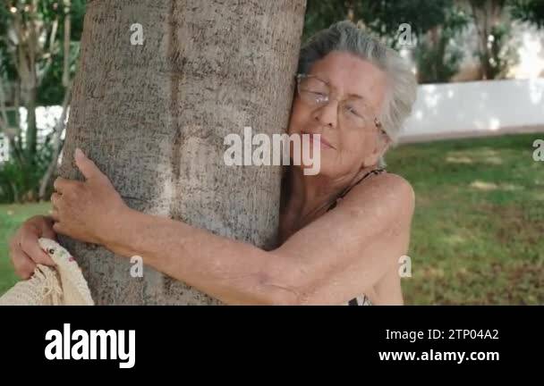 old 90s woman hugging a tree with love for nature . Happy and serene ...