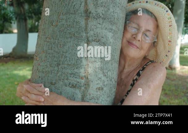 old 90s woman hugging a tree with love for nature . Happy and serene ...