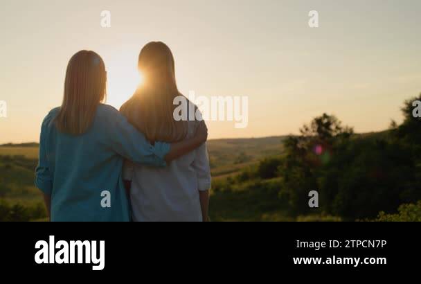A woman hugs her teenage daughter and together they watch the sun go ...