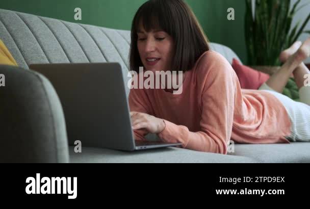 Caucasian woman lies comfortably on the couch with her laptop ...