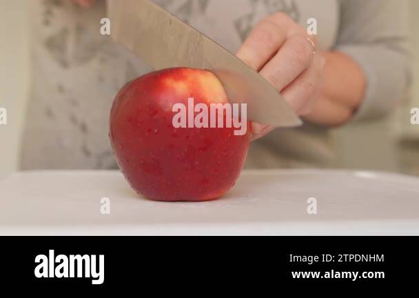 woman uses sharp kitchen knife to cut ripe large red apples into slices ...