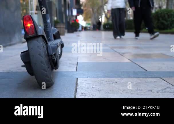 Electric scooter standing on the street sidewalk, with lit red stop ...