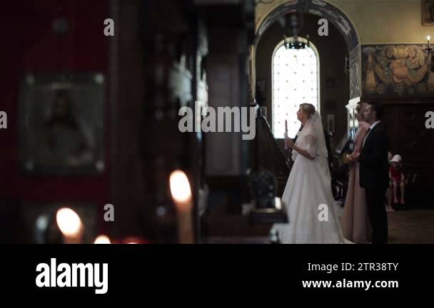 Bride and groom stand with candle at wedding ceremony in orthodox