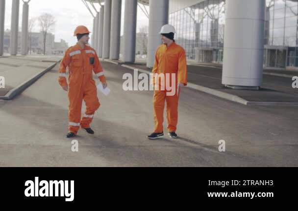 Two construction workers in orange uniform giving high five. They look ...