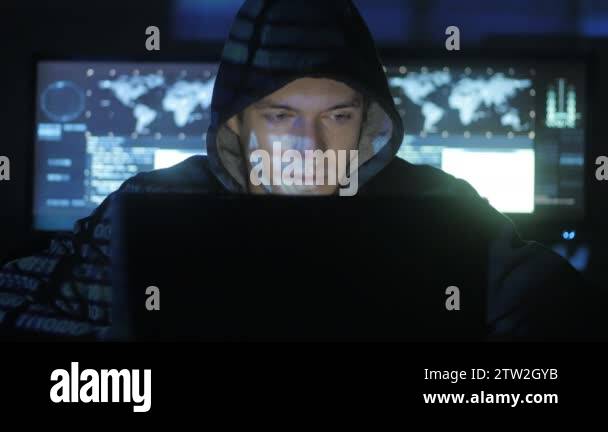 Man geek hacker in hood working at computer while blue code characters ...
