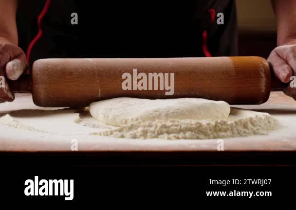 Sprinkled flour drops onto dough being rolled with a rolling pin by a ...