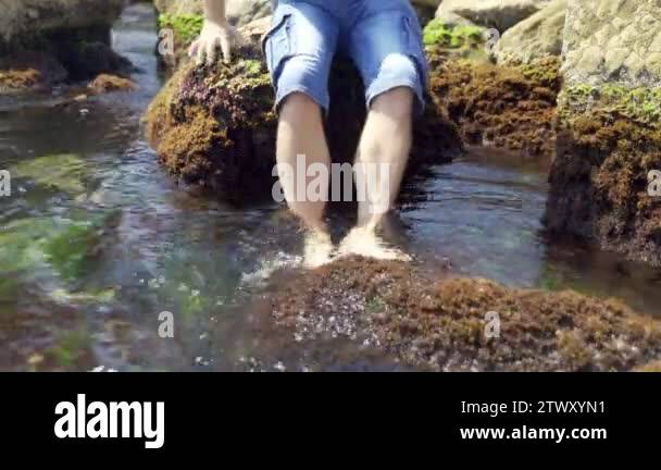 Men's feet are washed by sea waves. The barefoot of the guy stands on a ...