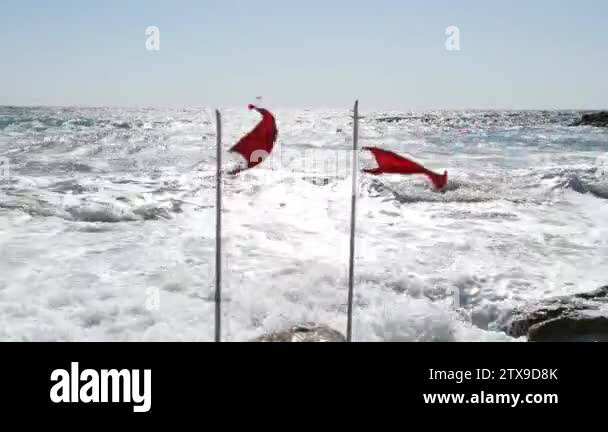 Two beach warning red flags splashing on wind. Stormy sea threat ...
