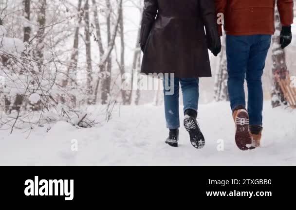 Back view of loving couple feet walking in a park on snowfall. Man and ...