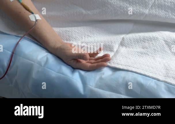 Hand of helpless patient lying on hospital bed, dropper in arm, person ...