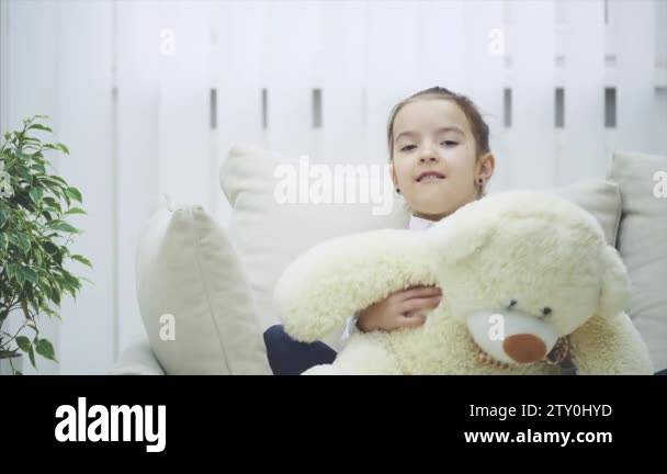 Cute little girl sitting on the sofa, hugging her teddy-bear Stock ...