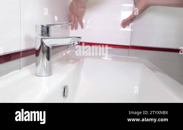 Worker hands turning on the water tap in a freshly finished new bathroom, showing the water ...