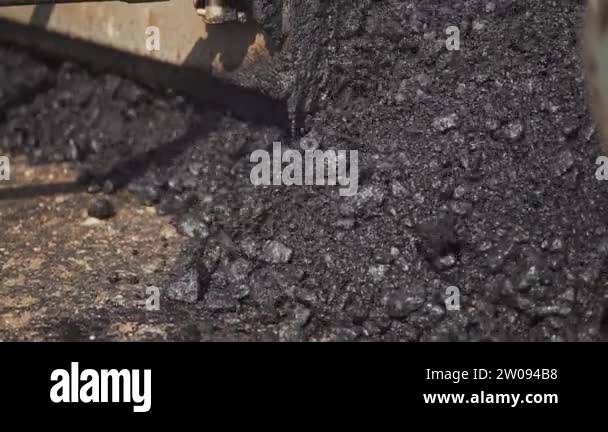 Close-up of hot asphalt pouring out the paver machine to the road ...