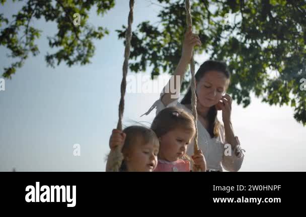 Mother shaking two small sisters on a swing with rope handles Stock ...