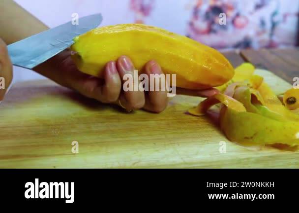 Young woman cleans and cuts mango. Girl peeling mango and hold it in ...