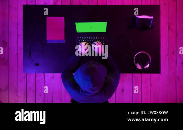 Hacker in hoodie typing code in program using laptop dark studio. Green ...