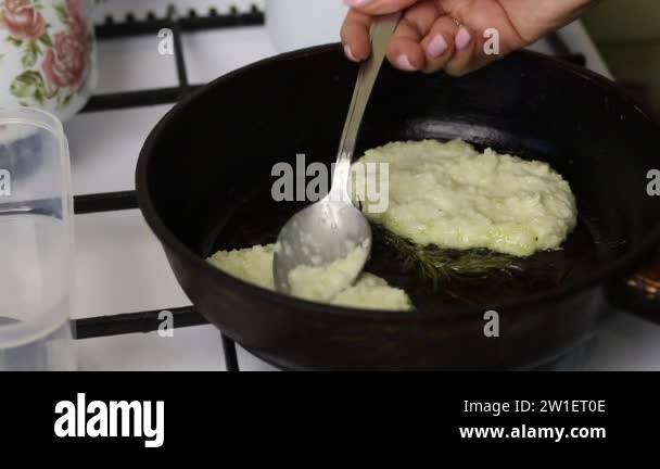 Woman fries pancakes. A woman puts mashed potatoes on a hot pan. Nearby