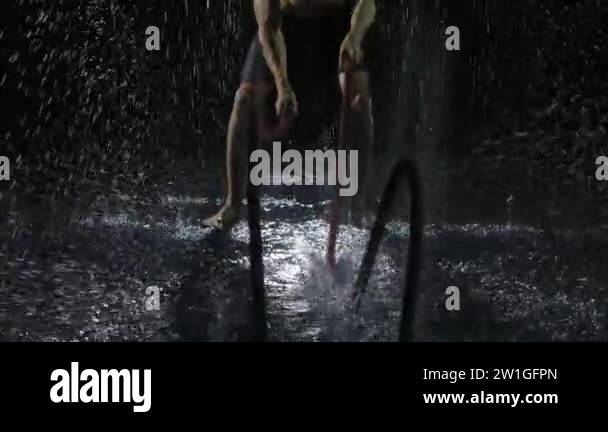 Athletic man trains intensely with battle ropes. The ropes hit hard ...