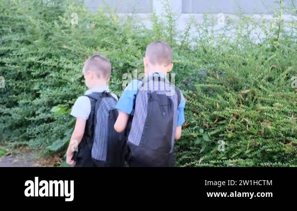 two boys, schoolchildren in black school uniforms with backpacks go to ...