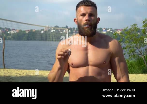Bodybuilder smokes a cigarette. Young bearded athletic bodybuilder plays  sports outdoors