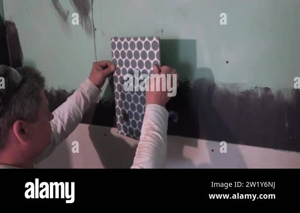 View of tiler man apply wall tile around hot and cold water pipes in bathroom ...