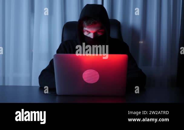 Man hacker face looking at computer screen. Male in black mask and hood ...