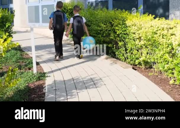 two boys, schoolchildren in black school uniforms with backpacks go to ...