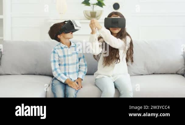 Caucasian small cute kids in VR glasses sitting on white sofa in living ...