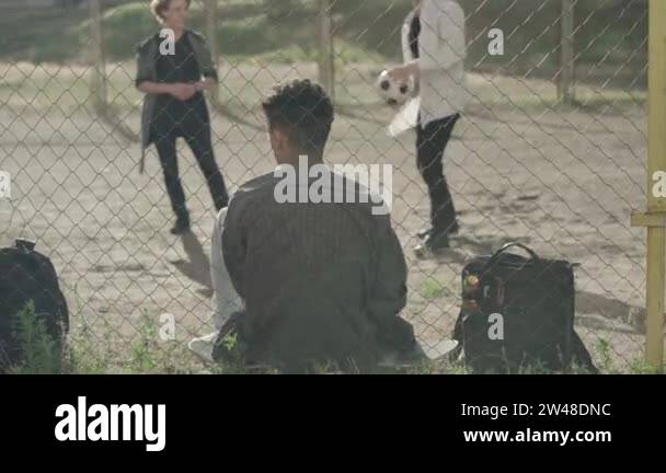 Back view of African American bullied man sitting at mesh fence as ...