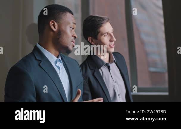 Two serious young businessmen multiracial colleagues standing in office ...