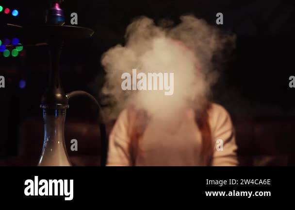 Young woman smoking at dark shisha lounge bar on dark room background