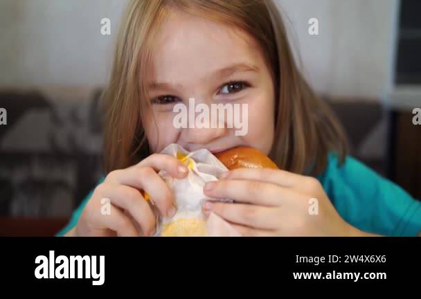 Funny little girl eats a delicious burger in a cafe. food for children ...