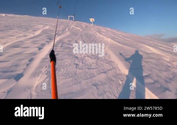 Snowboarder being pulled uphill by a t-bar drag lift at a ski resort ...