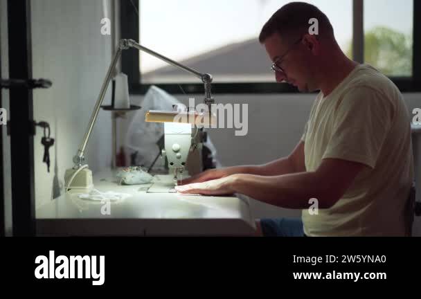 Young man watching a tutorial while using the sewing machine to make ... image.