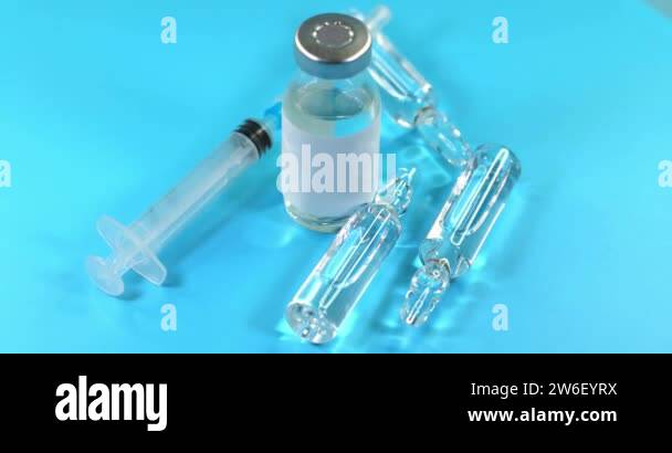 Glass vial filled with blue liquid vaccine and syringe rotate on ver ...