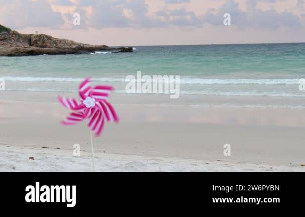 Pink pinwheel toy spinning on white sand beach, two colorful wind ...