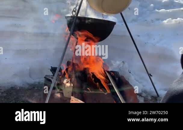 A tourist pot hangs over a campfire in winter, cooking on a fire in ...