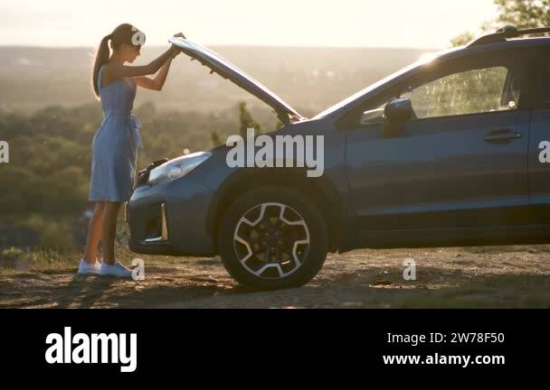 Stranded young woman driver standing near a broken car with popped up ...