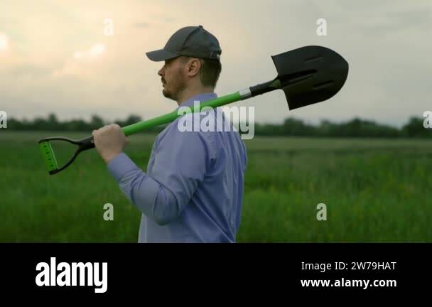 Farming concept. A farmer with shovel in his hands walks across field ...