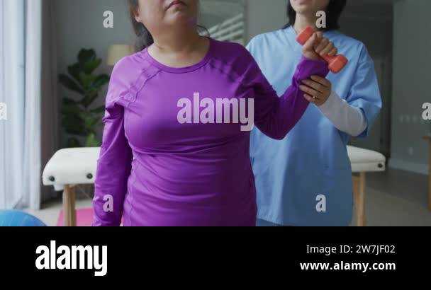 Asian Female Physiotherapist Helping Female Patient Exercise Arms With Dumbbells At Surgery 3474