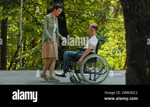 Disabled man in a wheelchair rides to his female friend and hugging her ...