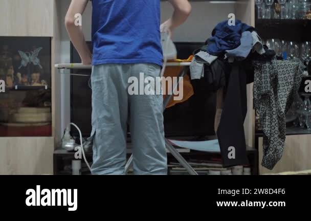 a boy ironing a T-shirt with an iron. housework. theres a pile of