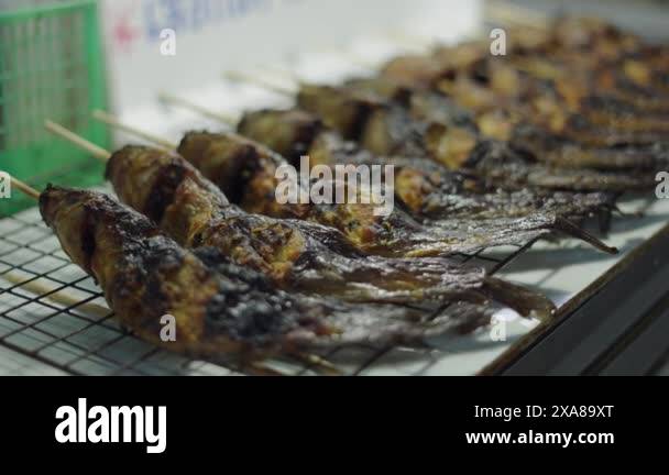row of cooked fish in a row with a long wooden stick through its body ...