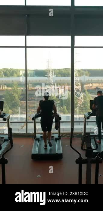 Three sporty guys, two men and woman running on treadmills in a gym ...