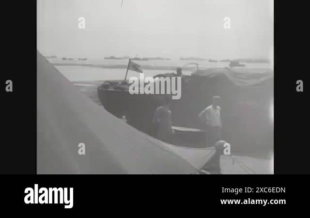 1945 - A DUKW drives on the Okinawa beach, landing craft carrying ...